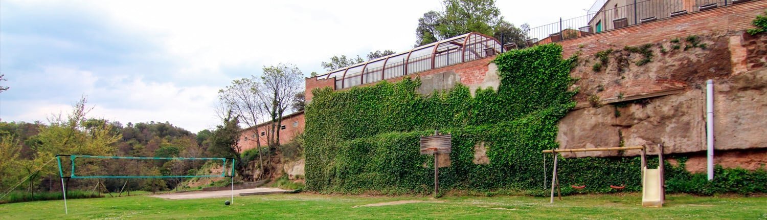 Zona ajardinada amb gronxadors, cistella bàsquet i red de volei de cal Masover de Barbats